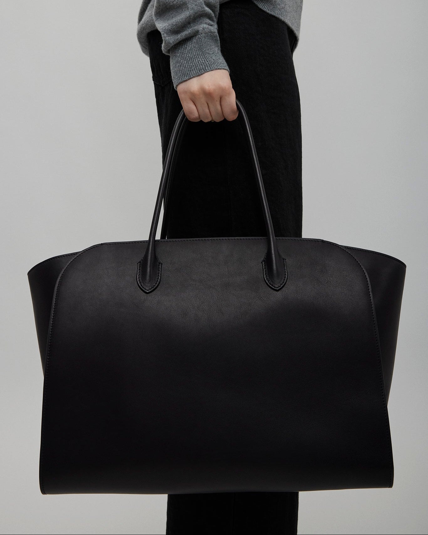 Person holding a black leather bag against a plain background