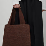 Person holding a brown woven bag against a plain background