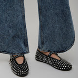 Black studded flats worn with blue jeans on a neutral background