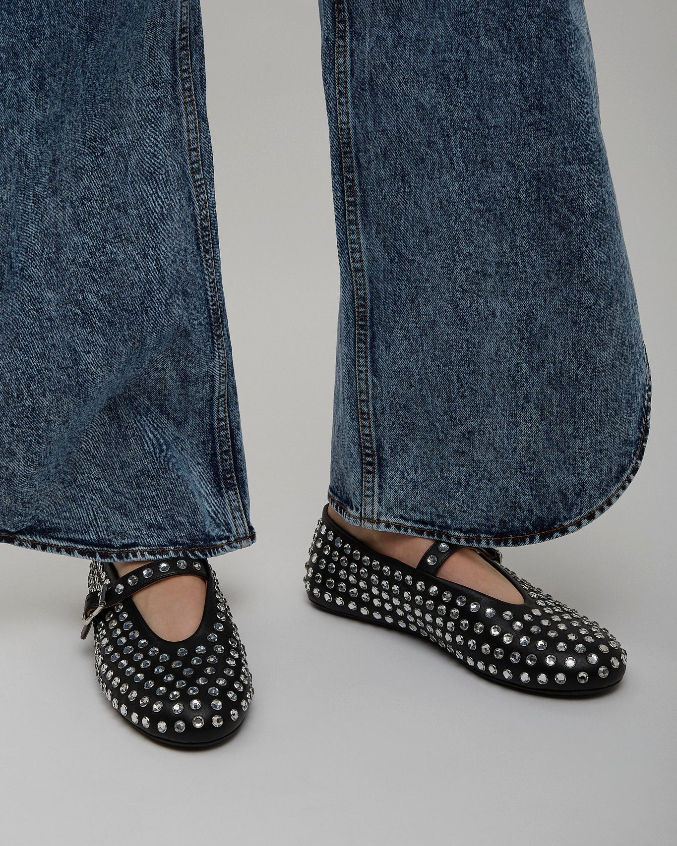 Black studded flats worn with blue jeans on a neutral background