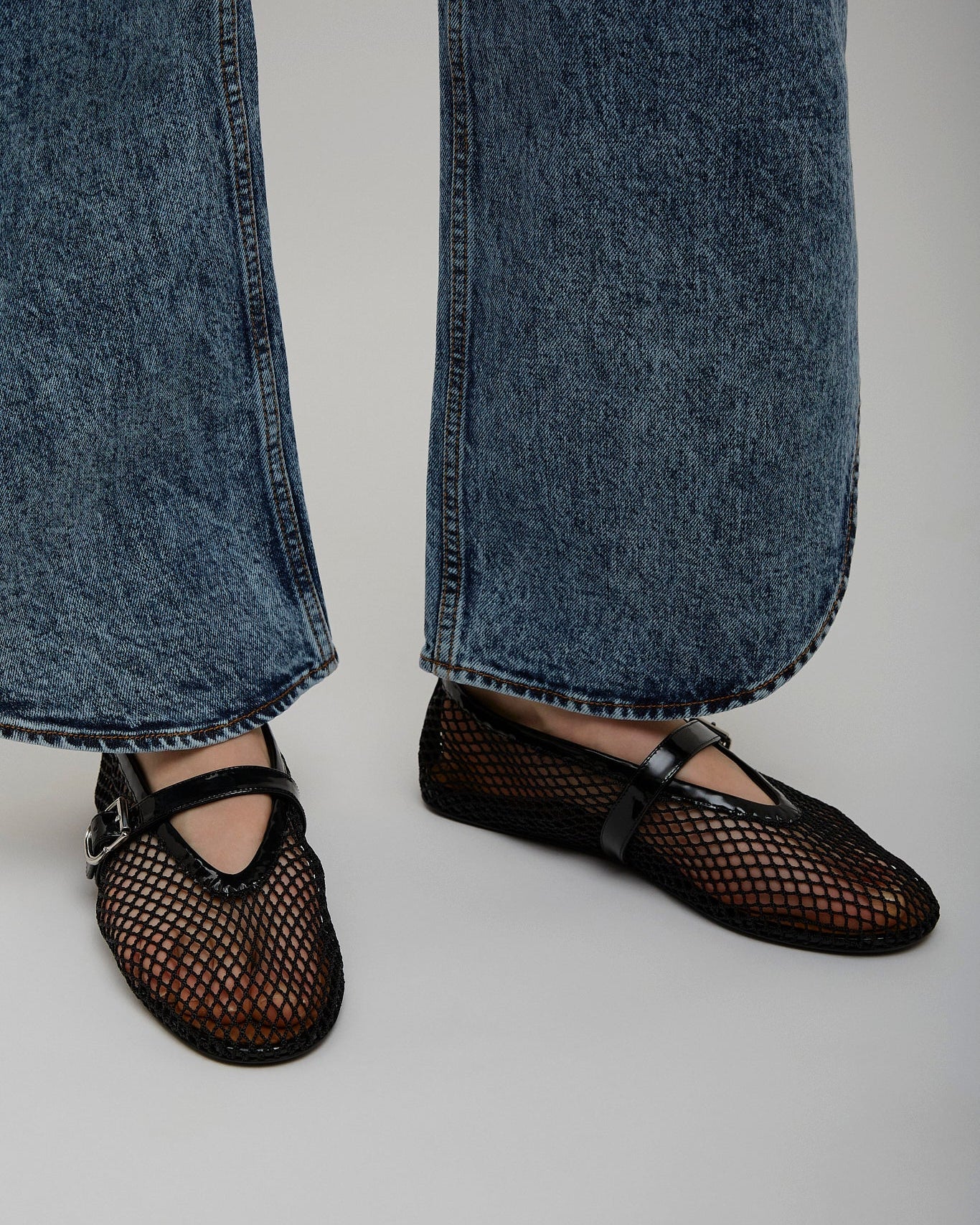 Person wearing black mesh shoes and blue jeans on a plain background