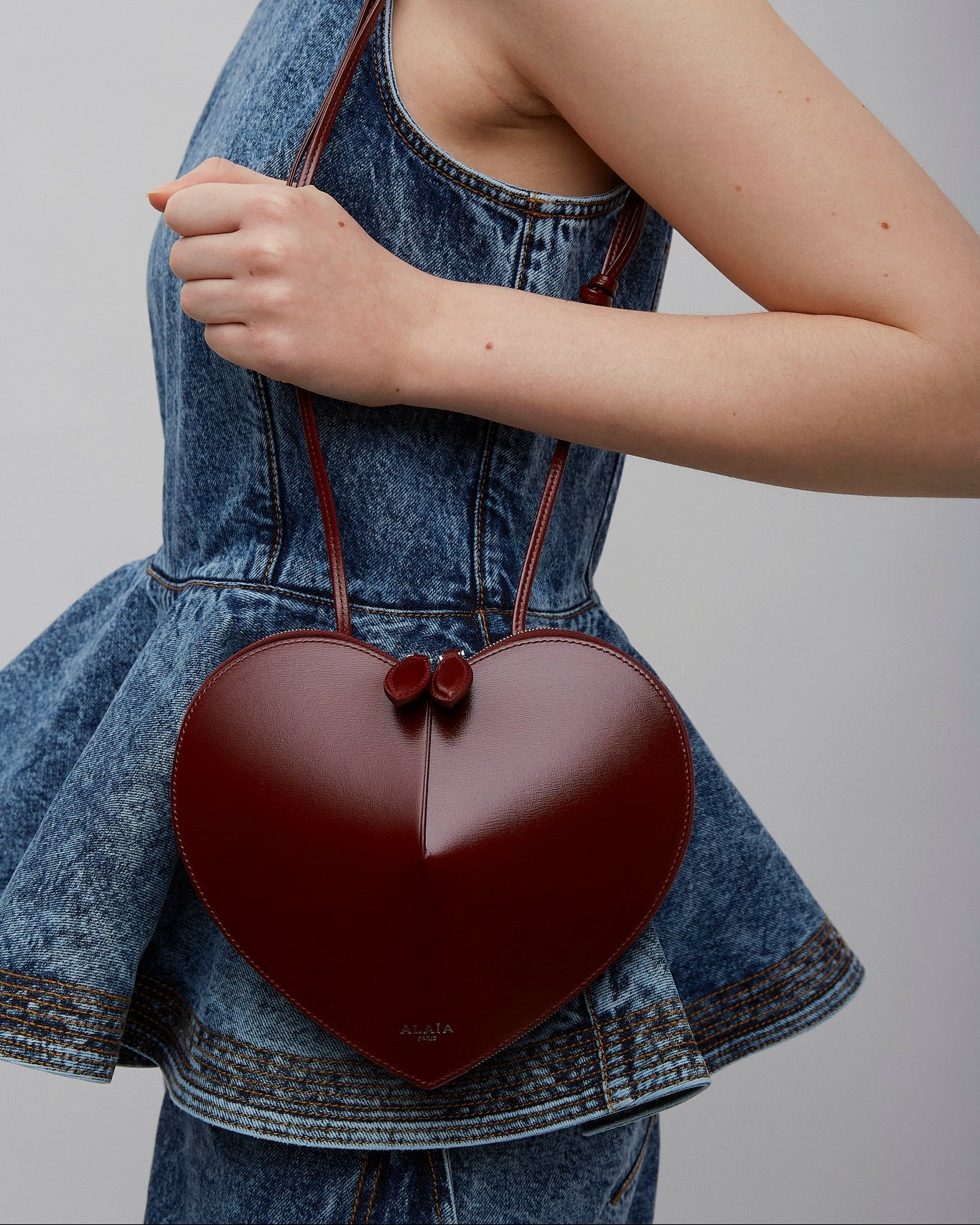 Heart-shaped handbag held by a person wearing a denim outfit on a plain background