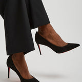 Black high-heeled shoes worn with black pants on a light gray background