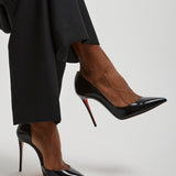 Black high-heeled shoes worn with black pants on a light gray background
