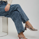 Person wearing blue jeans and metallic shoes sitting on a white background