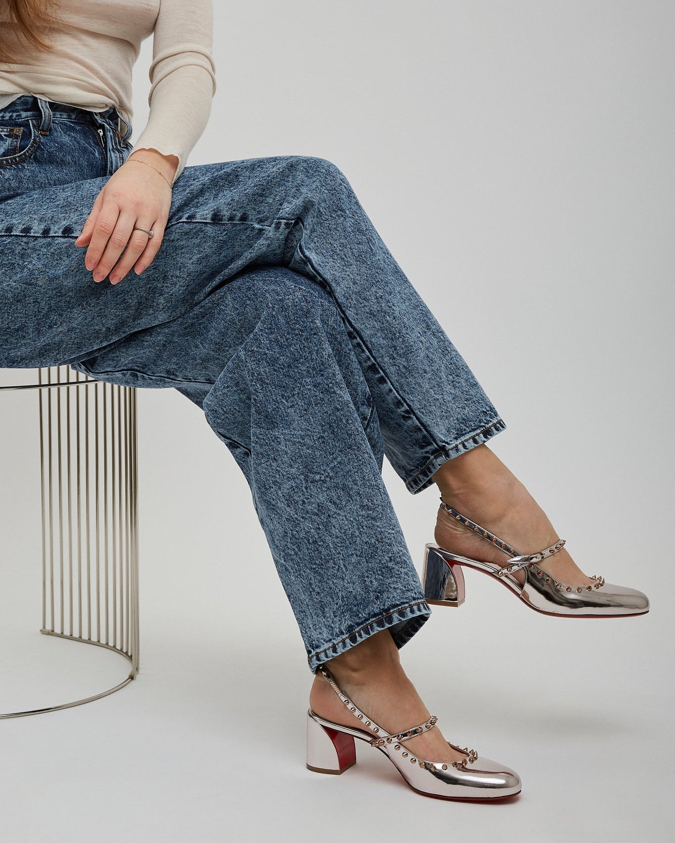 Person wearing blue jeans and metallic shoes sitting on a white background