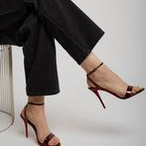 Person wearing black high-waisted jeans and red high-heeled shoes on a white background