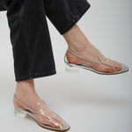 Clear sandals worn with black jeans on a plain background
